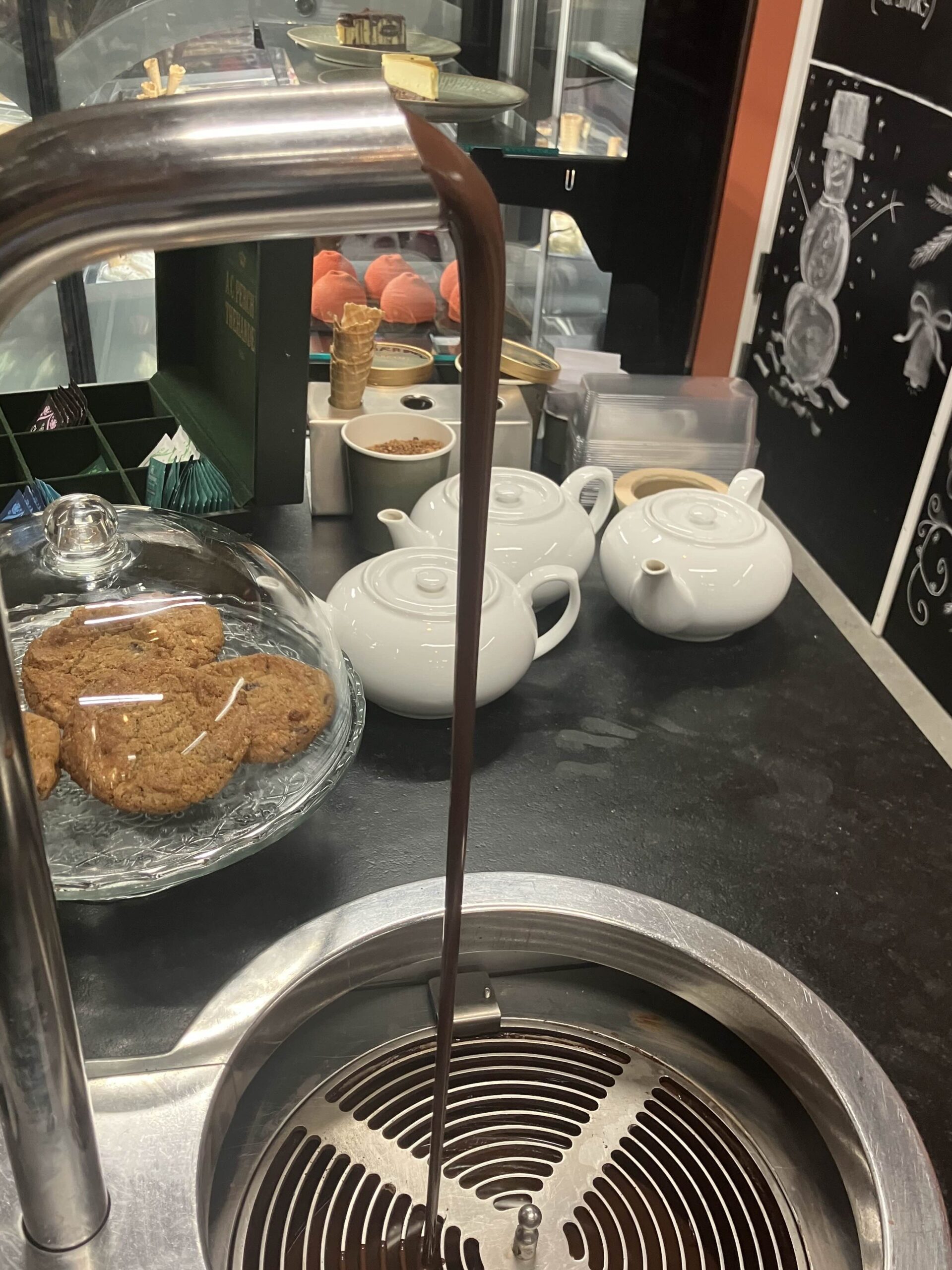 En chokolade hane med løbende lækker chokolade i en lokalt chokolade butik, med kager og display i backgrunden.
